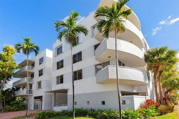 Front view of a multi-story building with balconies and palm trees.