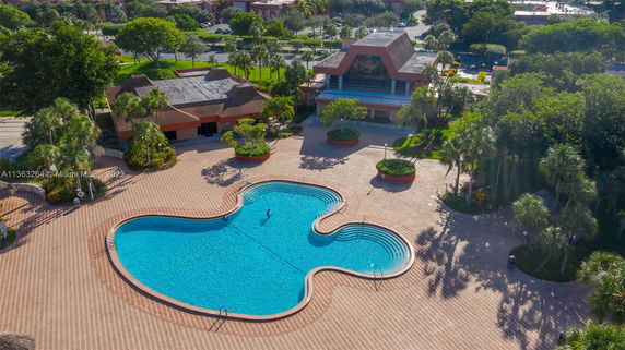 Outdoor area with a large, uniquely shaped swimming pool surrounded by a tiled deck and trees.