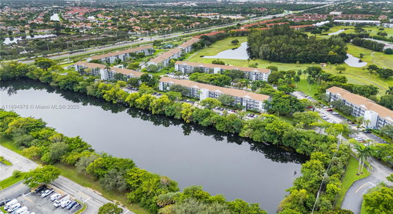 Aerial panoramic view of residential buildings surrounded by greenery, with a river in the foreground.
