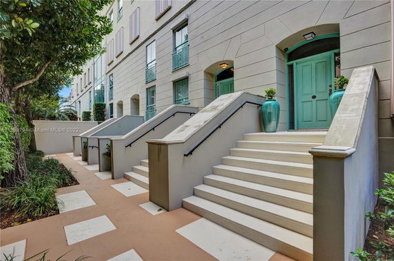 Front view of a multi-story building with stairs leading to green entrance doors.