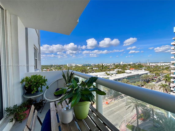 View from a balcony showing a cityscape with multiple buildings and clear blue sky.