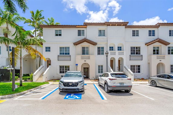 Front view of a three-story residential building with white facade and brown roof.