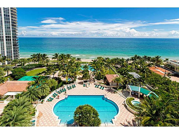 Wide angle view of pool area and oceanfront setting with lush greenery.