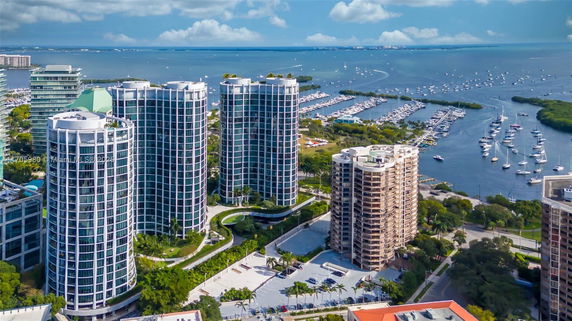 Aerial view of tall cylindrical buildings near a marina with numerous boats docked in the water.