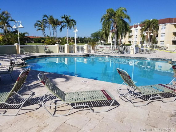Outdoor swimming pool area with lounge chairs and surrounding palm trees.