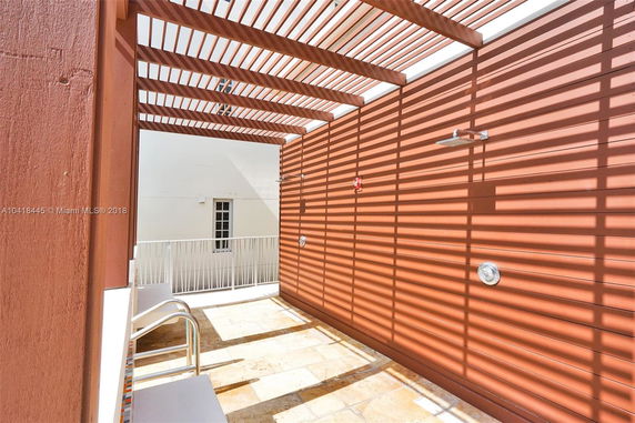 Rooftop area with wooden slats providing shade, a shower head, and railing.