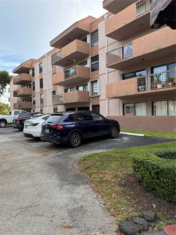 Front view of a multi-story residential building with several parked cars.