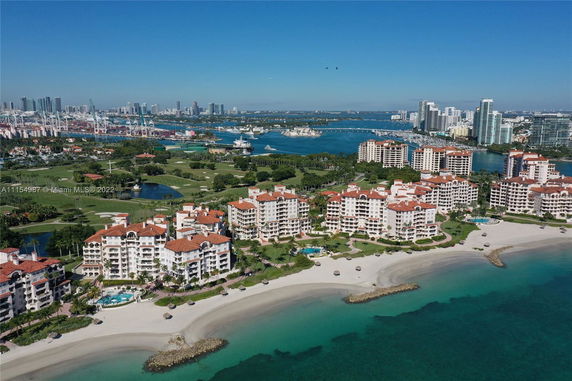 Aerial view of multiple beachfront condominium buildings with red roofs situated along a sandy coastline, with a city skyline visible in the background.