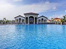 Large outdoor swimming pool in front of a building with arched doorways and a red roof.
