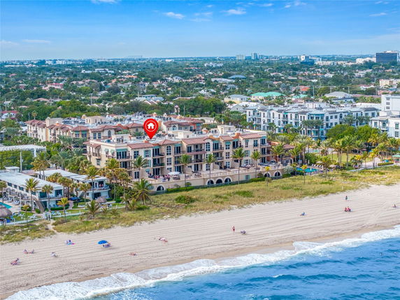 Aerial view of a beachfront multi-story building complex with nearby residential areas.