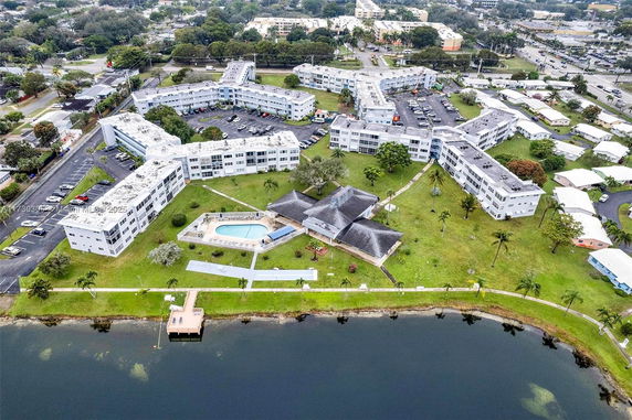 Aerial view of a multi-building apartment complex with a central swimming pool and landscaped grounds beside a body of water.