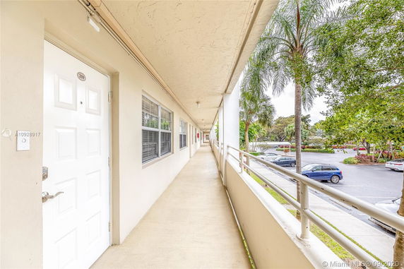 View of a building corridor with an adjacent parking lot and palm trees.