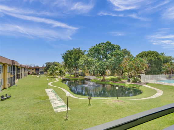 Panoramic view of residential complex with a grassy courtyard, pond, and walking paths.