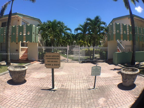 Front view of a condominium complex with gated entrance and palm trees.