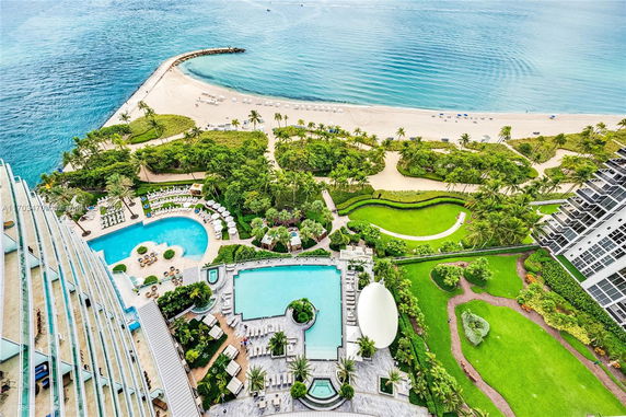 Aerial view of a beachfront property with swimming pools and lush gardens.
