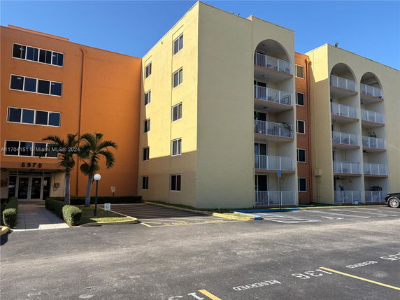 Front view of a multi-story residential building with balconies and a parking area.