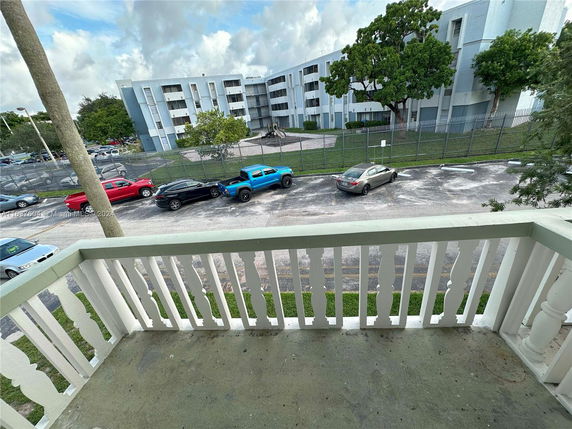 View from a balcony overlooking parking and a residential building.