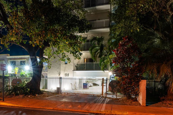 Front view of a multi-story building at night with balconies and surrounding trees.