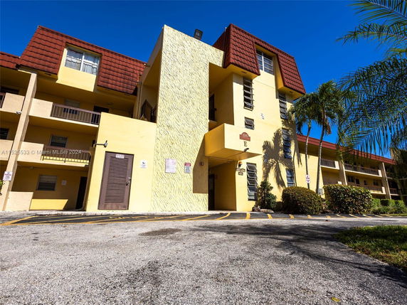 Front view of a multi-story residential building with balconies and a sloped red roof.