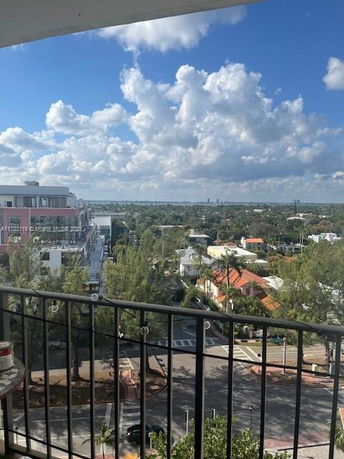 View from a balcony overlooking a cityscape with buildings and trees, under a blue sky with clouds.