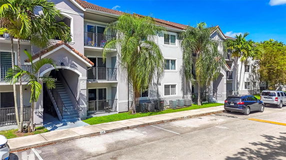 Front view of a multi-story apartment building with balconies and tropical landscaping.