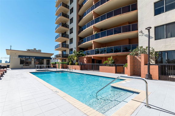 Outdoor view of a mid-rise residential building with balconies, adjacent to a swimming pool area.