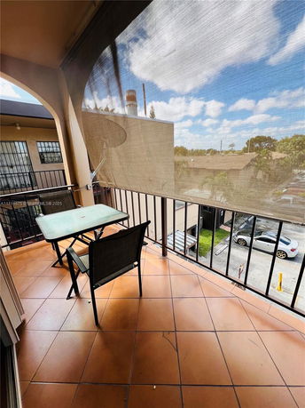 Balcony view with a table and chair, overlooking parking area and nearby buildings.