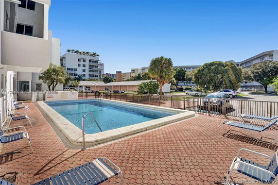 Outdoor swimming pool with surrounding lounge chairs and nearby buildings.
