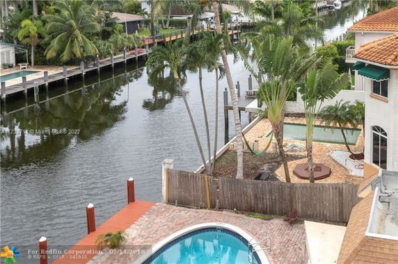 Aerial view of a canal-side residential area with a swimming pool and greenery.