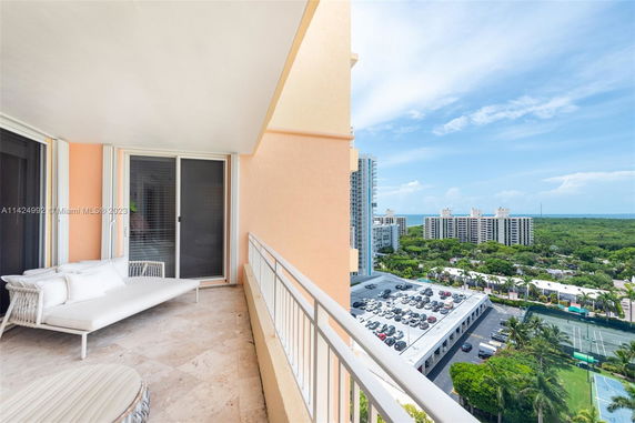 View from an apartment balcony overlooking buildings, parking, and greenery in the background.
