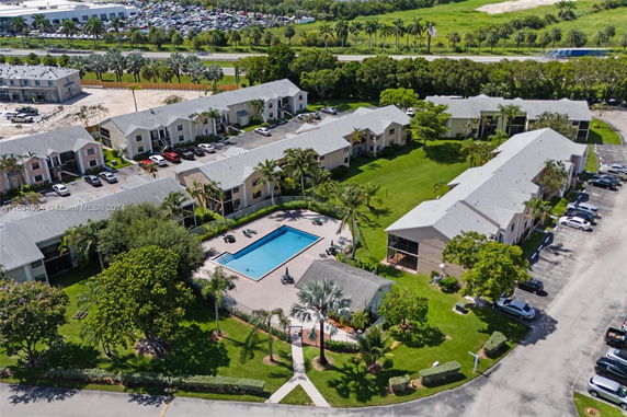Aerial view of a residential complex with multiple buildings, a central swimming pool, and surrounding greenery.