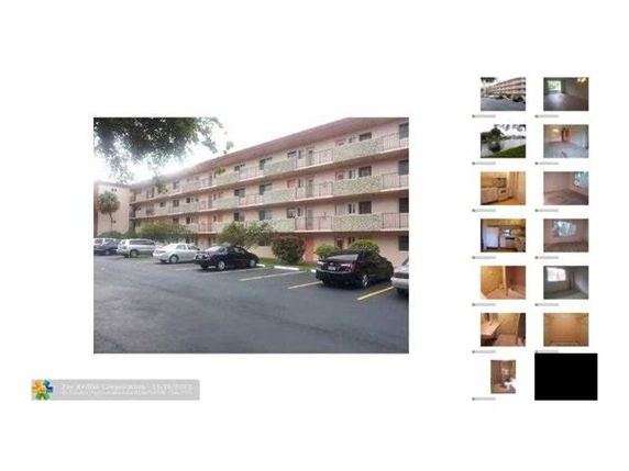 Front view of a multi-story residential building with balconies and a parking lot in front.