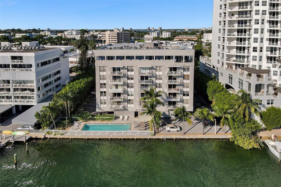 Front view of a multi-story building with balconies and a swimming pool by the water.