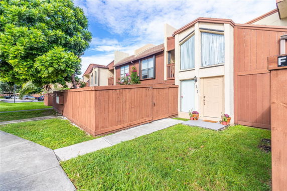 Front view of a multi-story townhouse with brown siding and a wooden fence.