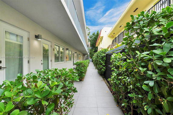 Exterior view of a walkway between two buildings with greenery and doors leading to apartments.