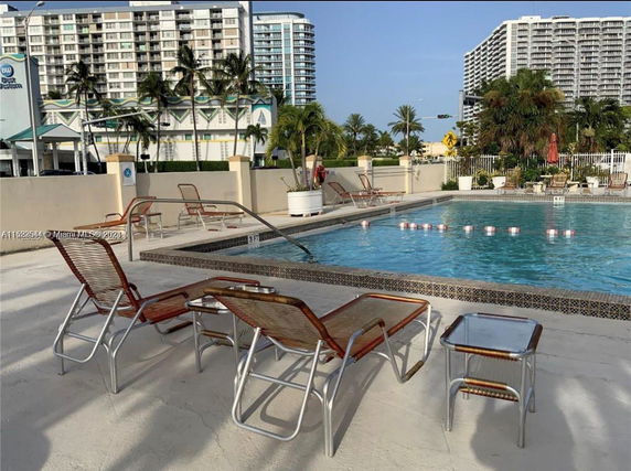 Outdoor swimming pool area with lounge chairs and nearby buildings.