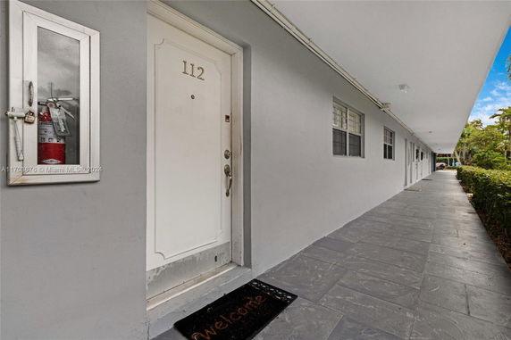 Front view of a building with a white door labeled 112 and a welcome mat.