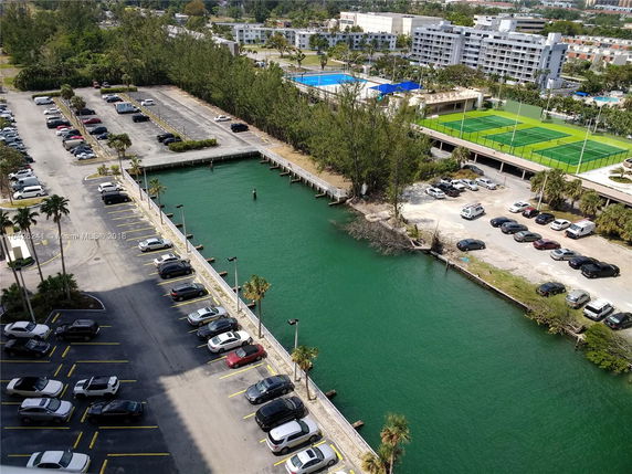 View of a parking lot and waterway with buildings and sports fields in the background.