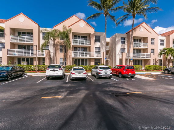 Front view of a multi-story apartment building with a parking lot in the foreground.