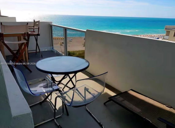Balcony view overlooking the ocean with chairs and a table.