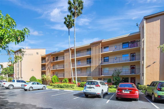 Front view of a multi-story residential building with balconies and adjacent parking spaces.