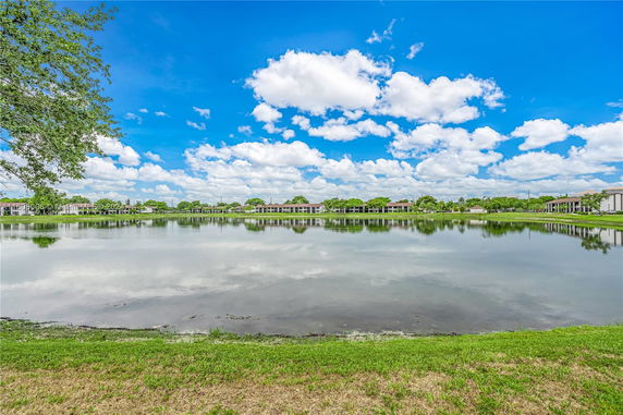 View of a lake with buildings in the background under a blue sky with clouds.