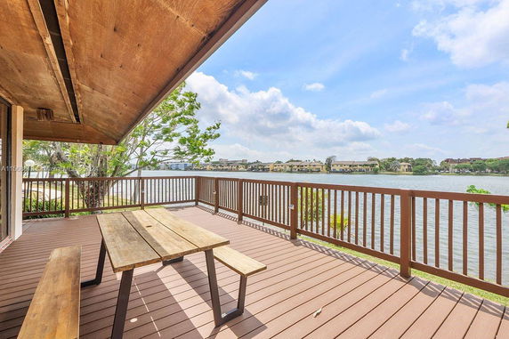 Outdoor deck with wooden table overlooking a body of water and distant buildings.