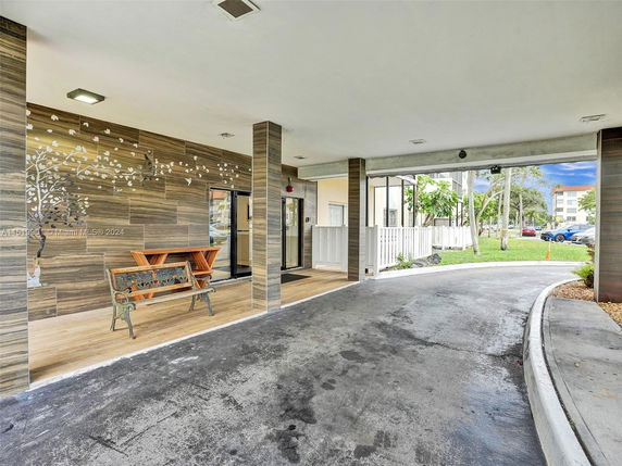 Outdoor area with covered parking space, decorative wall, and bench.