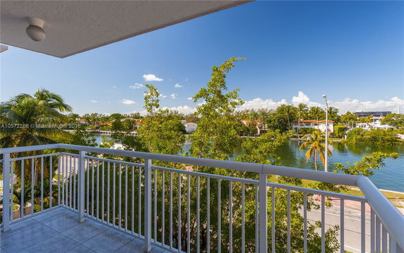 Balcony view overlooking water and lush trees with buildings in the background.