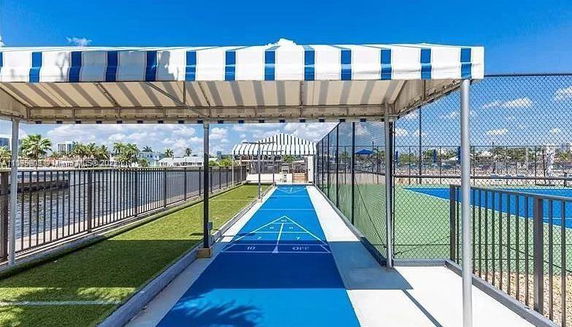 Outdoor recreational area with blue shuffleboard court and striped canopies.