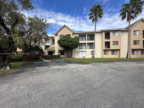 Front view of a multi-story residential building with balconies and a parking area in front.