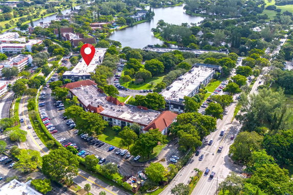 Aerial view of a residential complex surrounded by trees and roads, adjacent to a water body.