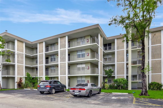 Front view of a multi-story apartment building with balconies and parking area.