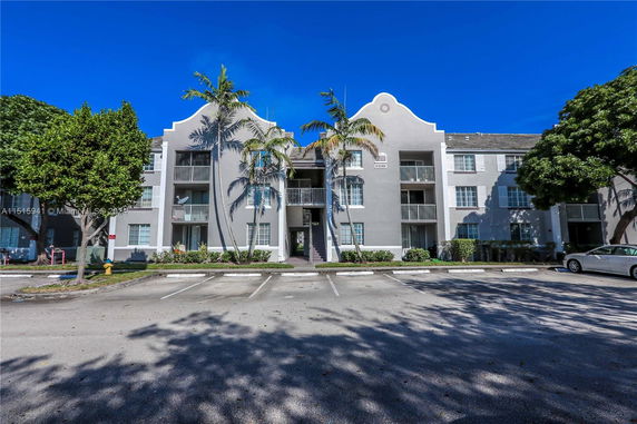 Front view of a three-story apartment building with balconies and palm trees.